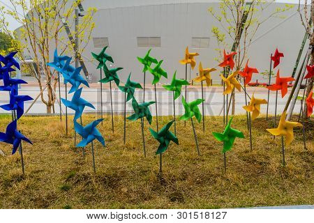 Muju,south Korea; May 1, 2019: Colorful Pinwheels In Trimmed Lawn With Competition Arena Building In
