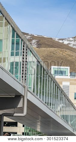 Clear Vertical Sunny Day View Of A Modern Building Exterior With A Glass Walled Skybridge