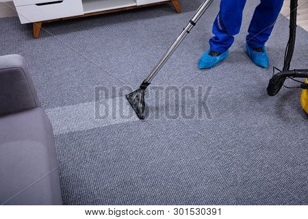 Low Section Of A Male Janitor Cleaning Carpet With Vacuum Cleaning In The Living Room