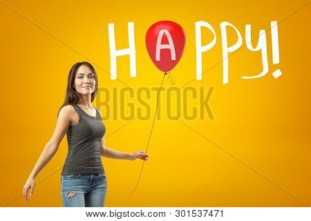 Young Smiling Girl In Casual Clothes Standing In Half-turn And Holding Red Balloon Against Yellow Ba