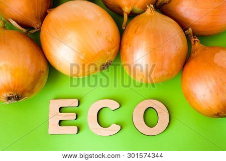 Onion Eco Product Or Food. Onions Bulb Are On Green Background With Text Eco Wooden Letters. Example
