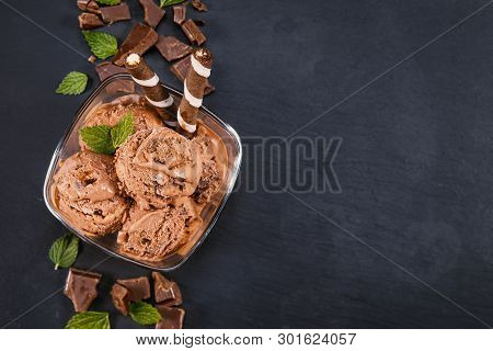 Scoops Chocolate Ice Cream In Glass Bowl With Wafer Sticks, Cone And Chocolate On A Black Slate Boar