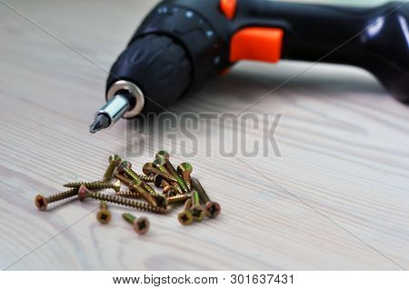 Electric Screwdriver And Screws On A Wooden Table.