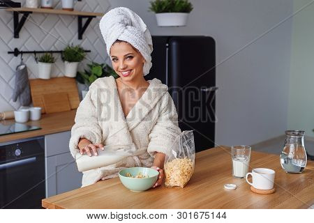 Close Up Young Woman In Bathrobe Pours Milk In Dep Plate With Corn Flakes. Pretty Girl Has A Healthy