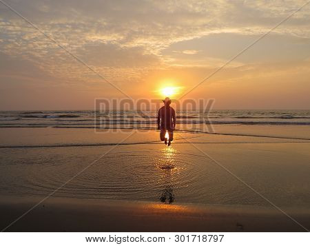 At Sunset, A Happy Man In A Hat Jumps Out Of The Water For Joy