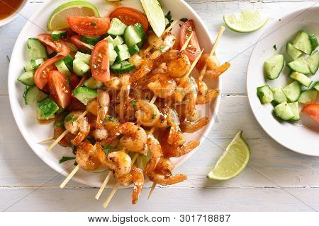 Close Up Of Prawns Skewers And Vegetables Salad From Sliced Cucumber And Tomatoes On White Plate Ove