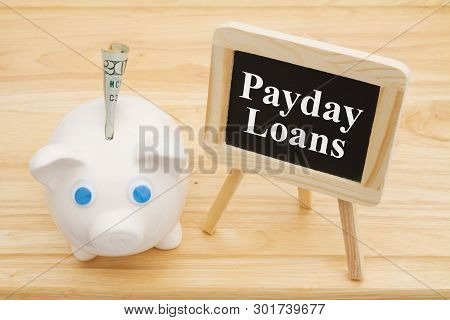 Learning About Payday Loans, A Piggy Bank With Money On A Desk With Chalkboard With Text Payday Loan