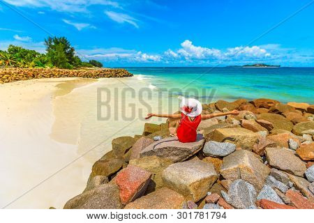 Carefree Tourist Woman Sitting On A Rock, Looks Turquoise Indian Ocean And Pristine Beach Of Anse Ke