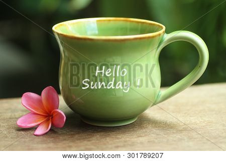 Green Ceramic Cup Of Coffee With Hello Sunday Greetings On It And Beautiful Pink Balinese Frangipani