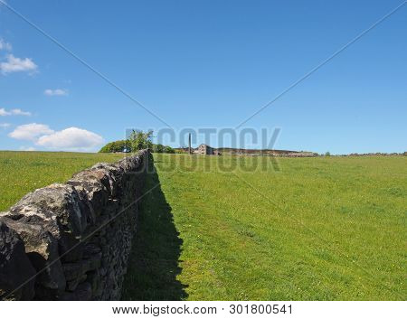 A Long Stone Wall In Perspective Bordering A Green Grass Meadow In Bright Spring Sunlight With A His