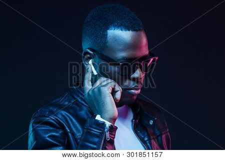 Serious African Male Listening To Music Or Answering Call Via Wireless Earphones At Night