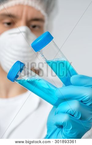 Young Male Medic Or Researcher Holds Up Three Medical Samples In Gloved Hand