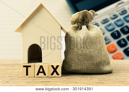 A Property Tax Or Millage Rate Concepts. Small House Model With Taxes And Money Bag On Table. Depict