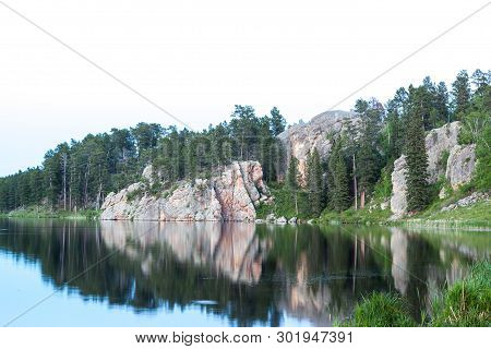 Calm Waters Of Stockade Lake Reflecting The Rocks And Trees Of A Dynamic Shoreline With An Isolated 