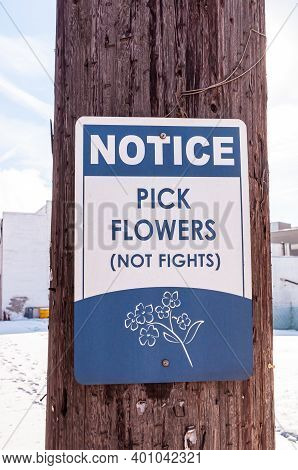 A Blue And White Metal Sign That Says Pick Flowers Not Fights On A Telephone Pole On A Sunny Winter 