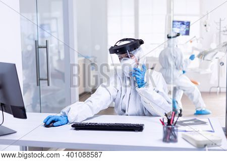 Dentist Nurse Dressed In Ppe In Stomatology Clinic During Covid-19 Discussing With Patient Over Phon