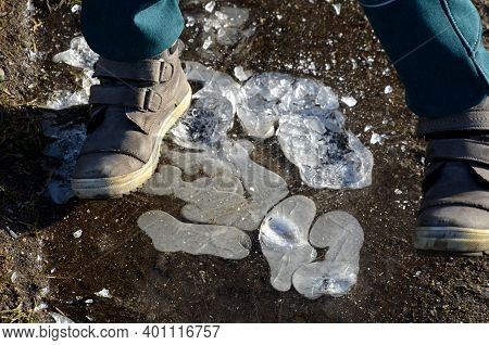 Little Boy Stomps On A Frozen Pool Where He Breaks The Heel Of Air Bubbles In The Ice. Frozen Roadsi