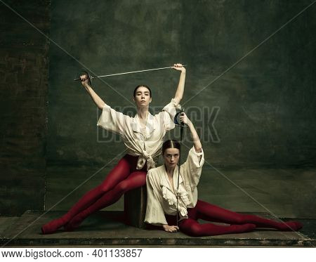 Flexibility. Two Young Female Ballet Dancers Like Duelists With Swords On Dark Green Background. Cau