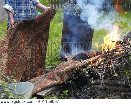A Man Burning Old Unwanted Carpet In A Backayrd, Focus In The Foreground