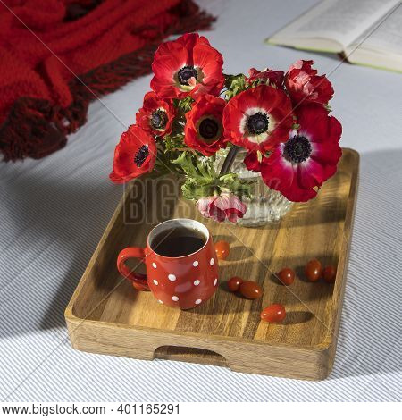 A Bouquet Of Red Anemones In A Glass Vase On A Wooden Tray On The Bed. White Polka Dot Cup With Tea.
