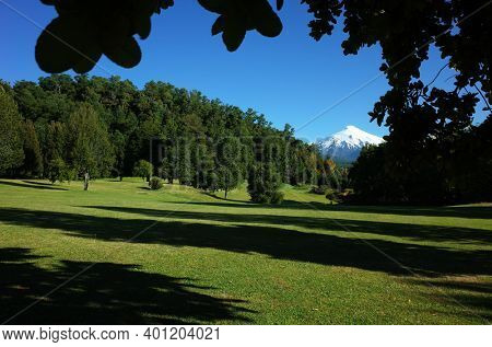 Nature of Chile. Beautiful landscape, sun and shadow, Green grass and forest on hill, Snowy cone of Villarrica volcano under blue sky in sunny day. Green environment, Pucon