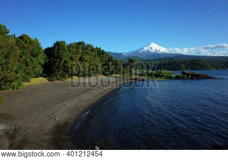 Nature of Chile, Beautiful landscape, Dark volcanic sand beach on Villarrica lake, snow capped Villarrica volcano under blue sky in sunny day. Green environment, Pucon