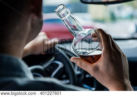 Cropped View Of Man Holding Bottle Of Alcohol While Driving Car, Blurred Foreground.
