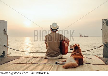 A Man Wear Straw Hat And Playing Guitar Music Song Near The Sea Sunset With A Dog Pet.
Travel, Vocat