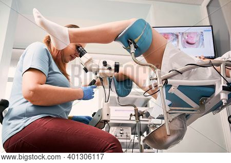 Side View Of Gynecologist Using Colposcope While Examining Woman In Gynecological Clinic. Female Pat