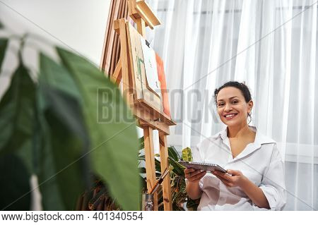 A Happy Beautiful American Woman Smiles At Camera While Sitting Near Easel