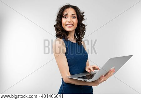 Close-up Of A Girl Office Employee In A Blue Dress Holding A Laptop In Her Hands On A White Studio B