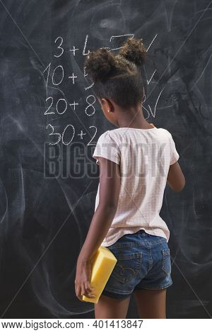 Beautiful Mixed Race Schoolgirl Standing In Front Of A Chalkboard, Solving Math Equations, Practicin