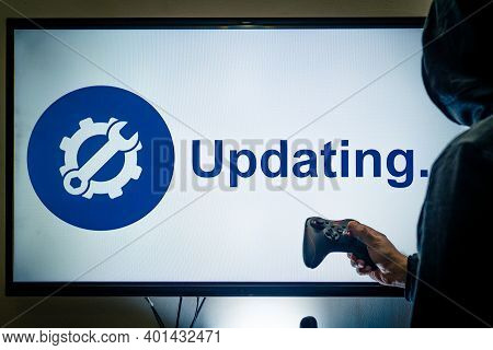 Hooded Man Holding A Gaming Controller In Front Of A Screen Showing An Updating Message For A Game O