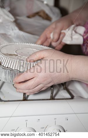 Woman Picking Up A Carryout Tin From A Stove With A Carryout Bag In The Background