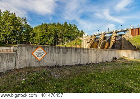 Large Rural Dam. Large Concrete Dam With Sign Warning Of Rising Water Levels. Located In Baraga Coun