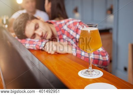 Selective Focus On A Glass Of Beer On Bar Counter, Young Man Sleeping Drunk At The Pub