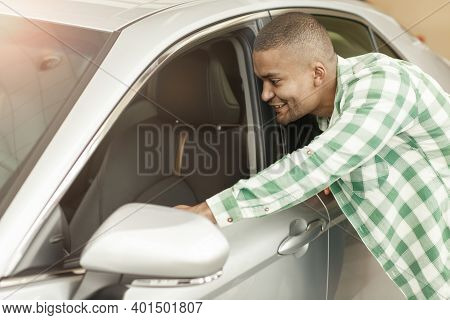 Happy Young African Man Looking Inside A New Car At The Dealership. Handsome Male Customer Examining