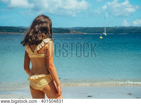 The Pictures Shows A Back View Of A Little Girl In A Bikini On The Beach With The Sea In The Backgro