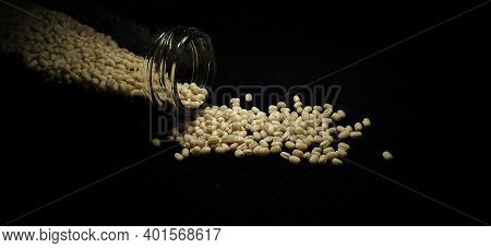 Closeup Of Urad Dal (white) In A Glass Container Spilled On A Isolated Black Background With Copy Sp