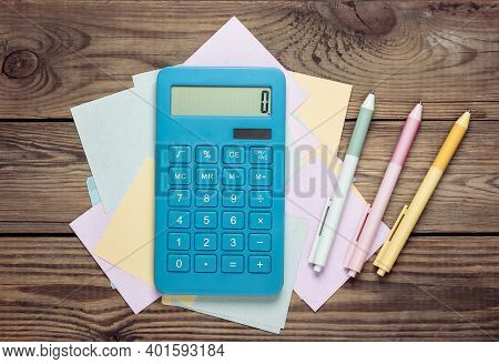 Calculator With Memo Papers And Colored Pens On A Wooden Table.