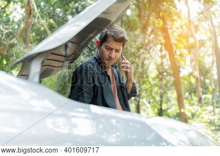Man Using Phone For Repair As Maintenance Service. Man Trying To Repair A Car Engine, Looking Inside