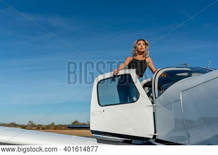 A gorgeous young blonde model poses outdoors with a single engine aircraft at a local airport