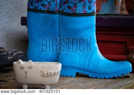 Old Dirty Rubber Boots Stand On The Wooden Floor Of A Country House Porch. Blue Rubber Country Golos
