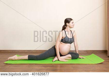 Beautiful Young Pregnant Woman Sitting On Mat In Yoga Pose At The Home. Pregnancy Yoga And Fitness C