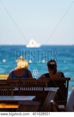 Two Unidentified Woman Sitting In Beach Cafe With Glass Of Rose Wine En Looking To Blue Water Of Gul