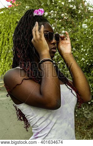 Vertical Shot Of A Young African Woman Dressed In A White Dress And Sunglasses Poses Next To Some Sm