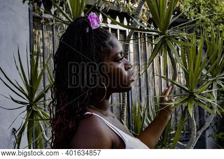 The Young African Woman Dressed In A White Dress Looks To One Side As She Rests Her Hand On A Tropic