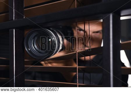 Private Detective With Camera Spying Near Window Indoors, Focus On Lens