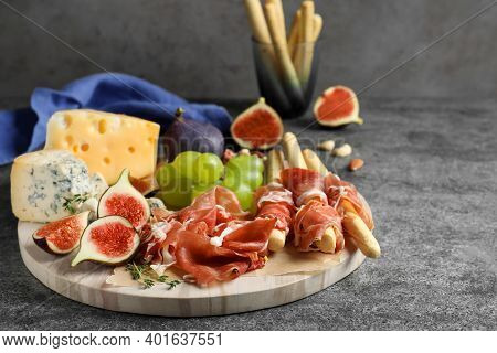 Board With Delicious Figs, Cheese, Grapes And Bread With Proscuitto On Grey Table