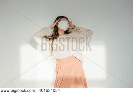 Denier Woman In A White Sunlit Room With A White Fabric Mask On Her Face.